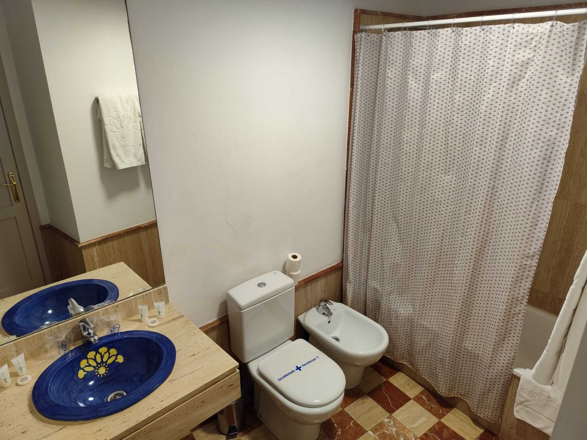 Een badkamer met een blauwe wastafel, toilet en douchegordijn.