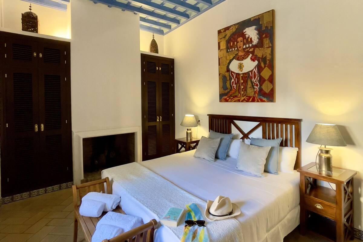 Une chambre à coucher avec un grand lit, une tête de lit en bois, une table de chevet, une lampe, un tableau au mur et une armoire.