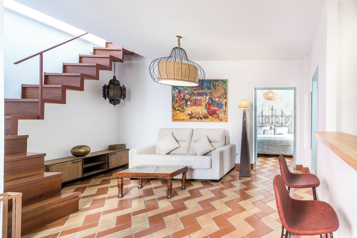Un salon moderne avec un escalier, un canapé blanc, une table basse en bois et un tableau coloré.