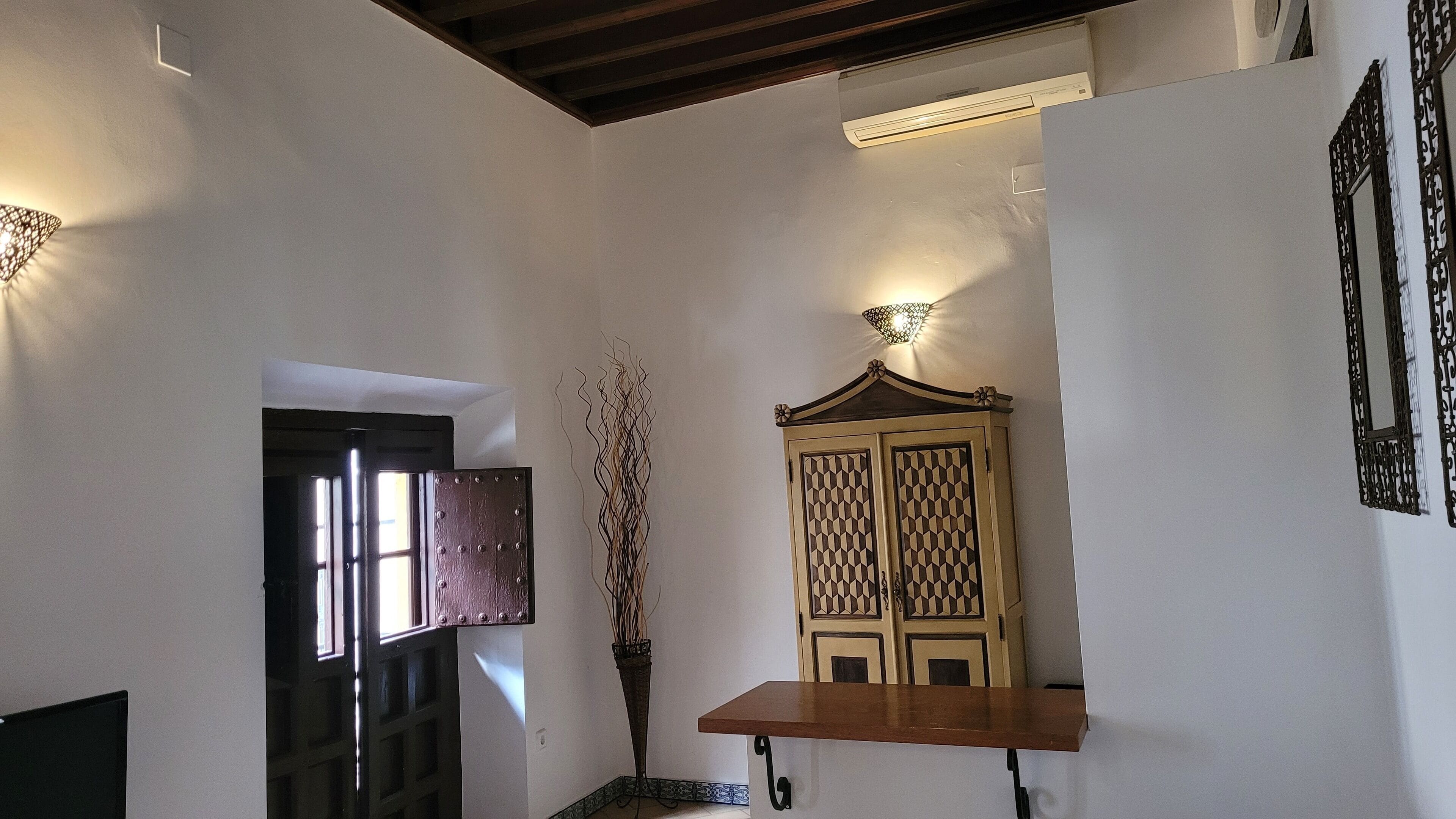Un couloir avec une porte en bois, un meuble décoratif et une étagère fixée au mur.