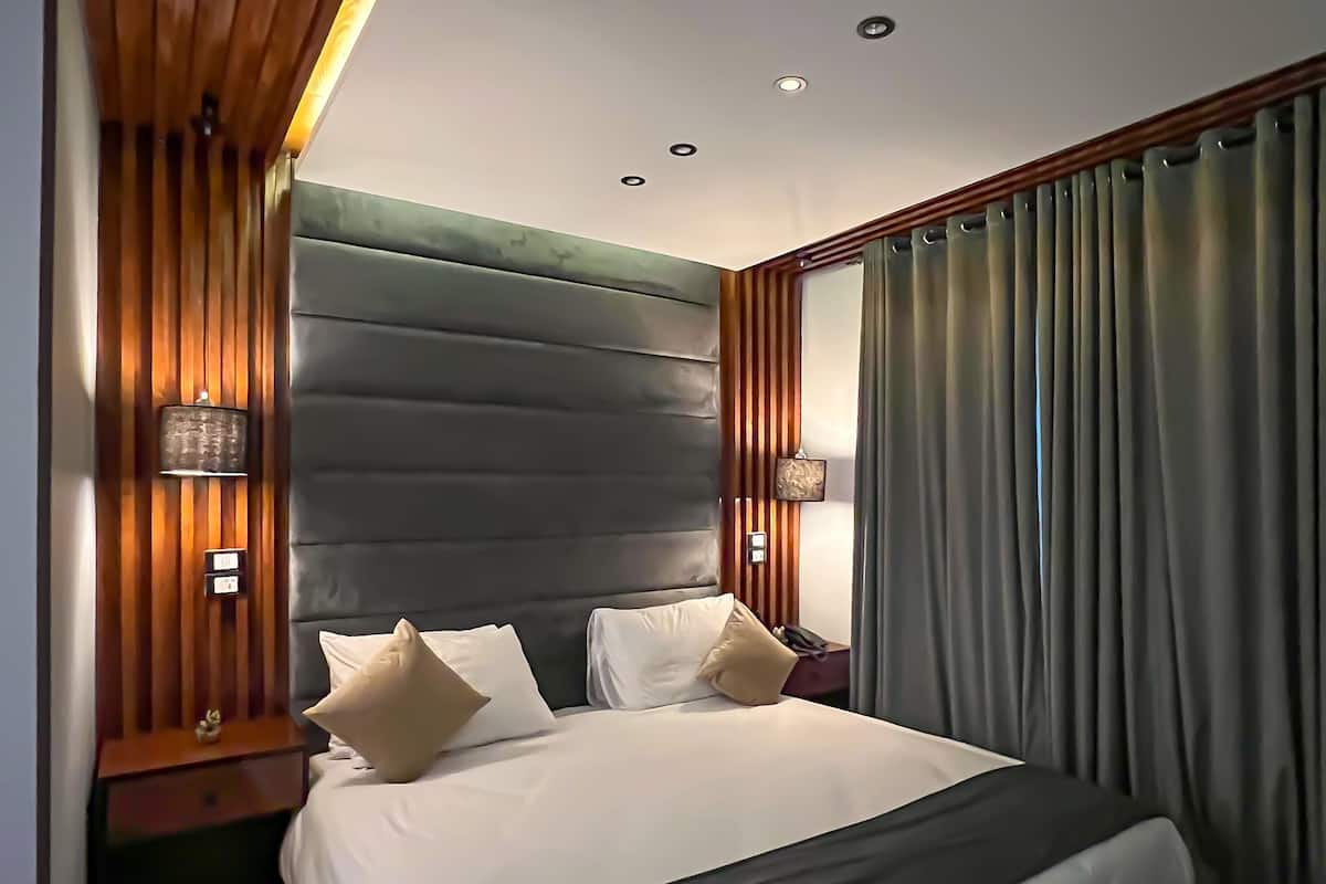 A modern hotel room with a large bed, wooden paneling on the walls, and a view of the city.