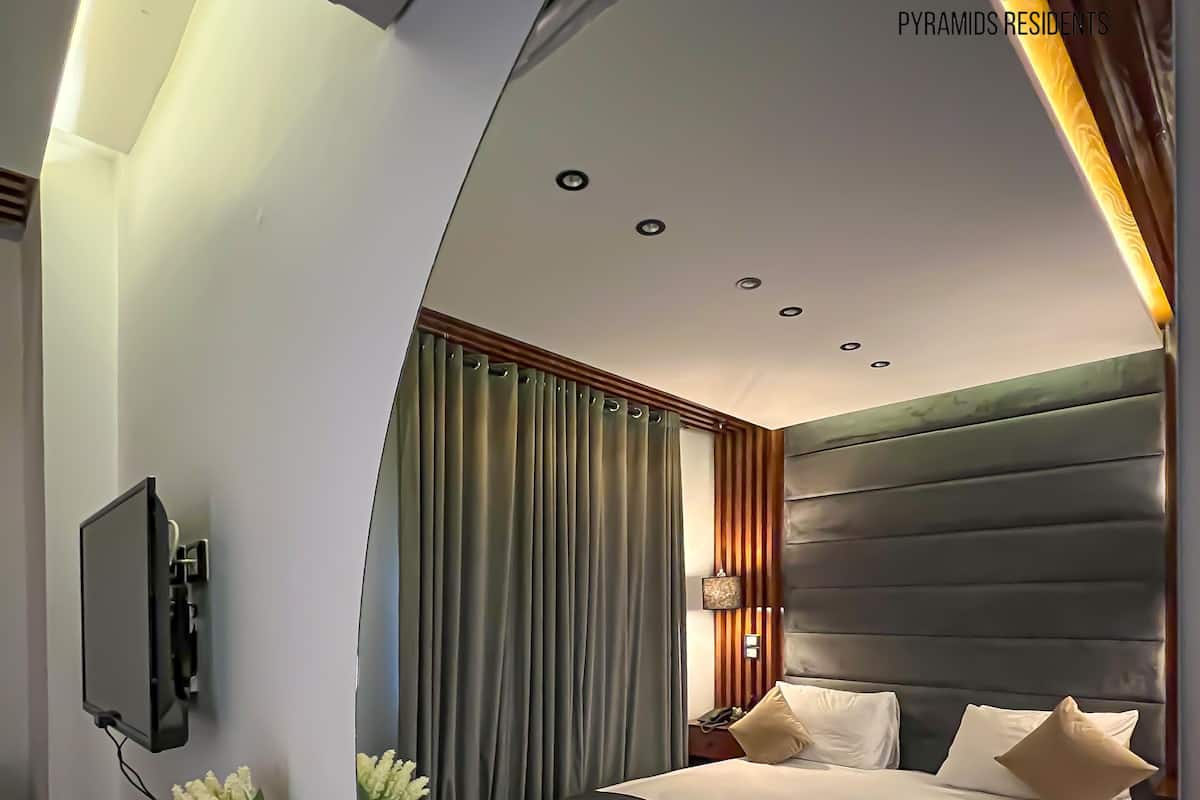 A modern hotel room with a large bed, a desk with a menu, and a TV mounted on the wall.