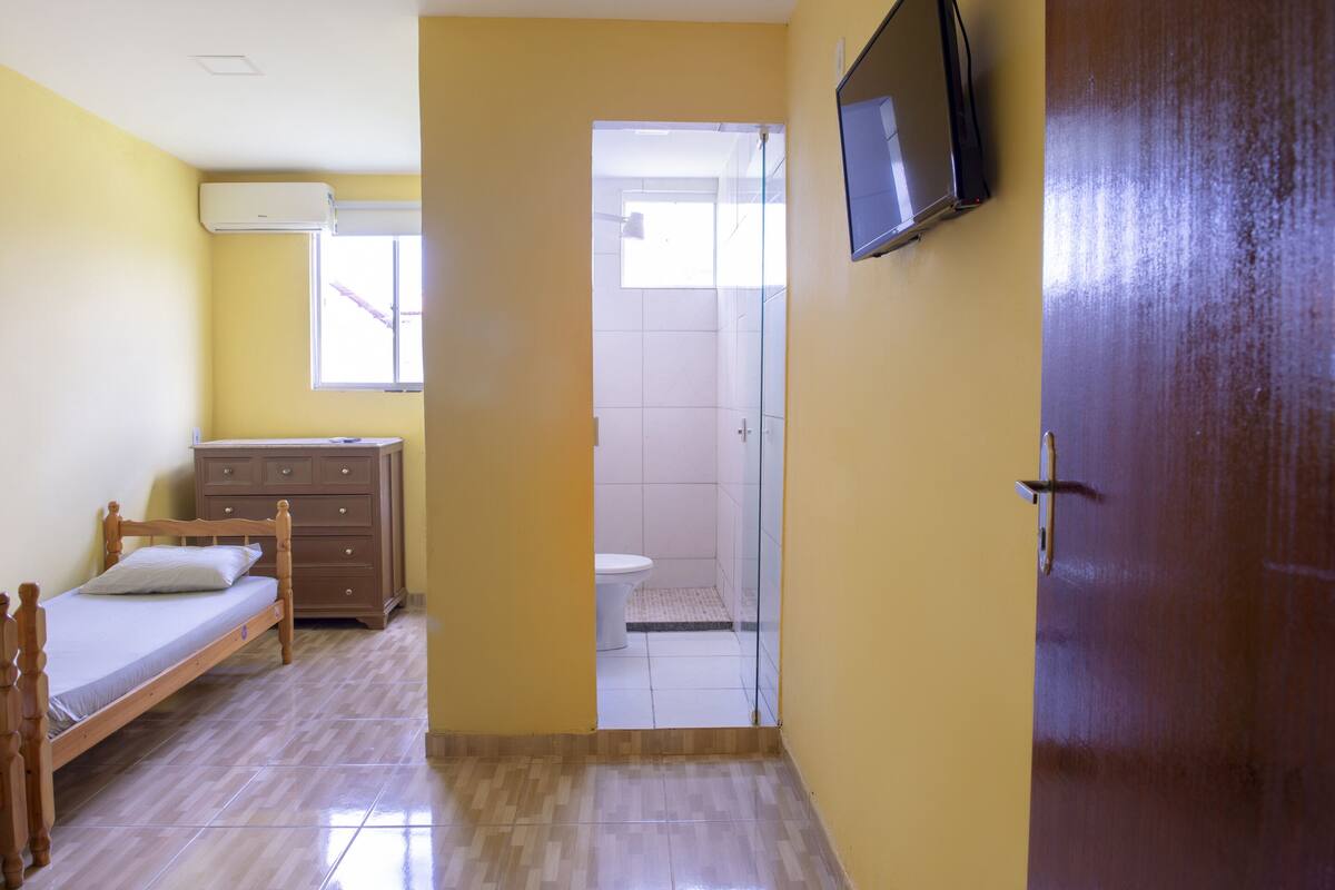 A bedroom with a wooden bed, a dresser, a TV mounted on the wall, and a door leading to a bathroom.