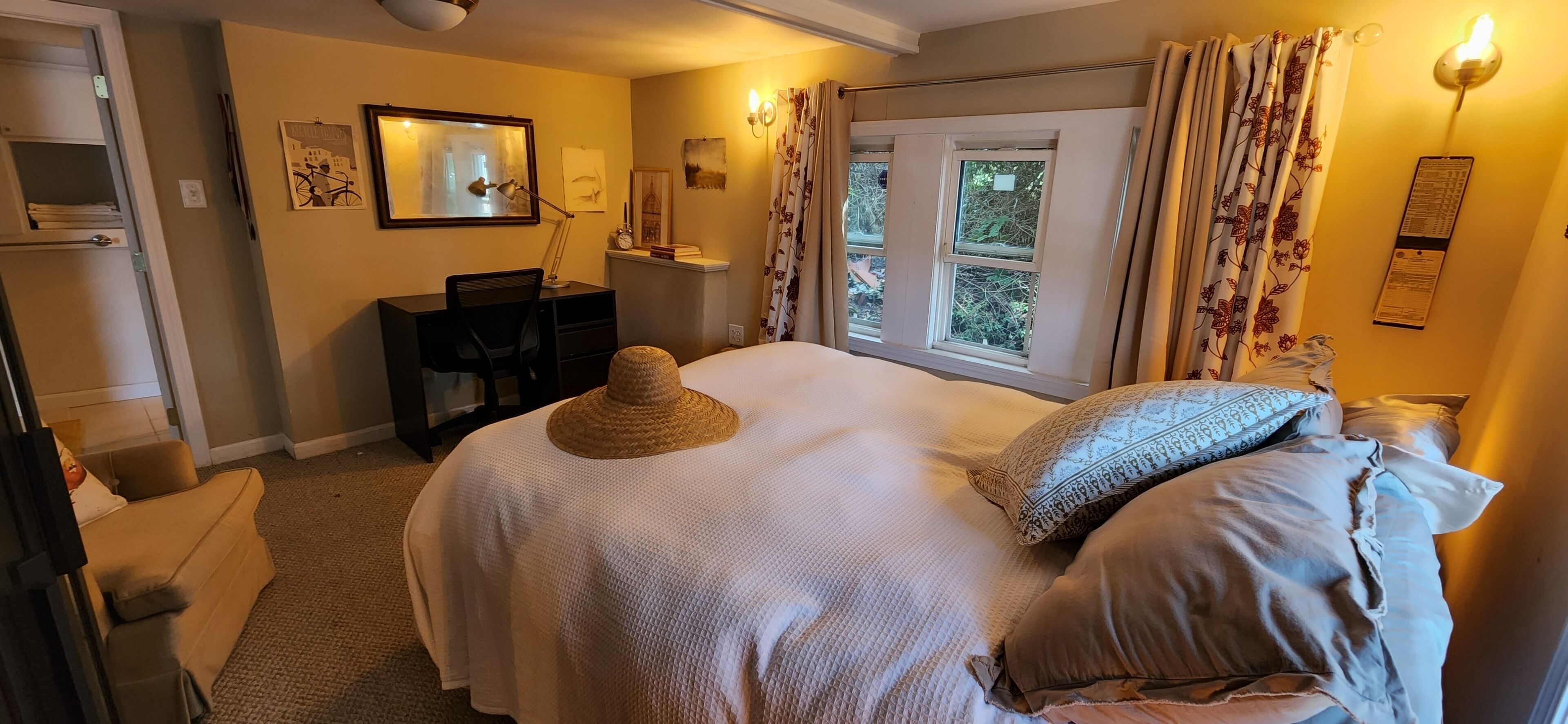 Un dormitorio con cama, escritorio, silla, ventana con cortinas e iluminación en la pared.