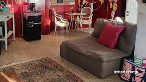 A cozy living room with a red brick wall, a vintage refrigerator, a small table with chairs, and a patterned rug. - Beach, marina, restaurants! 1 bedroom, living room, bath with private entrance! (Wareham)