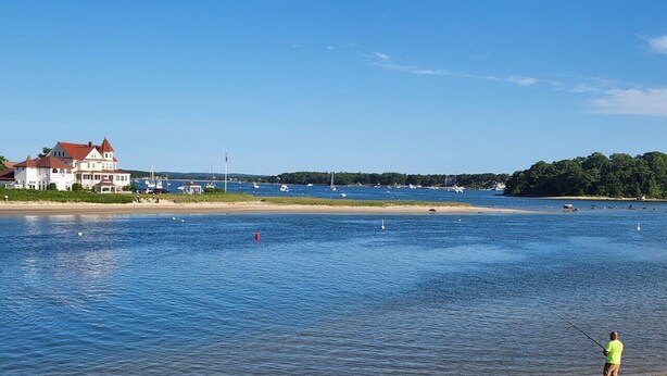 A waterfront property with a large house, a sandy beach, and a person fishing. - Beach, marina, restaurants! 1 bedroom, living room, bath with private entrance! (Wareham)