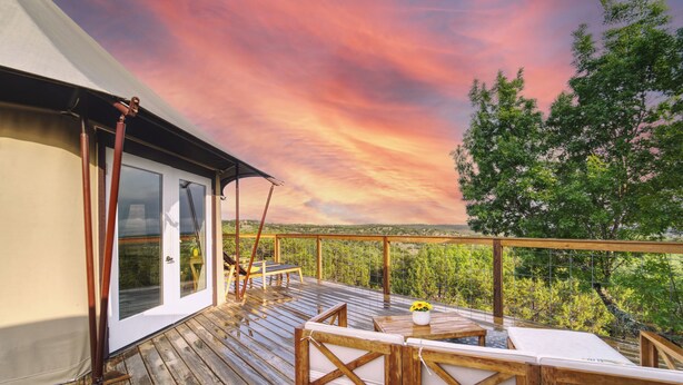 Eine Holzterrasse mit Sitzgelegenheiten im Freien, eine Glastür und eine schöne Aussicht auf Bäume und Hügel.