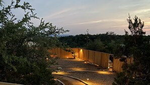 Ein gut beleuchteter Weg durch eine angelegte Grünfläche mit Holzzaun und einer Holzterrasse.