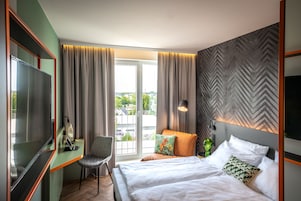 Camera d'albergo con un letto, una scrivania con sedia, una televisione e vista sull'esterno.
