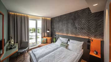 A modern hotel room with a large bed, a desk with a laptop, a chair, and a view of the city through the window.