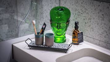 A bathroom counter with a green glass bottle, two cups, a toothbrush, and a bottle of hand soap.