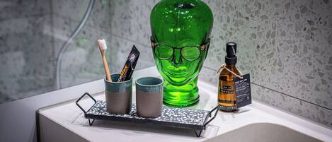 A bathroom counter with a green glass bottle, two cups, a toothbrush, and a bottle of hand soap.