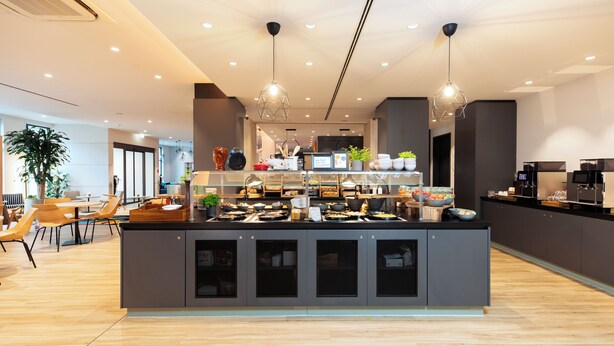Een moderne keuken met een centraal eiland, verlichting boven en een zithoek met stoelen en tafels.