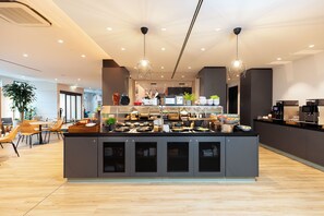 Een moderne keuken met een centraal eiland, verlichting boven en een zithoek met stoelen en tafels.