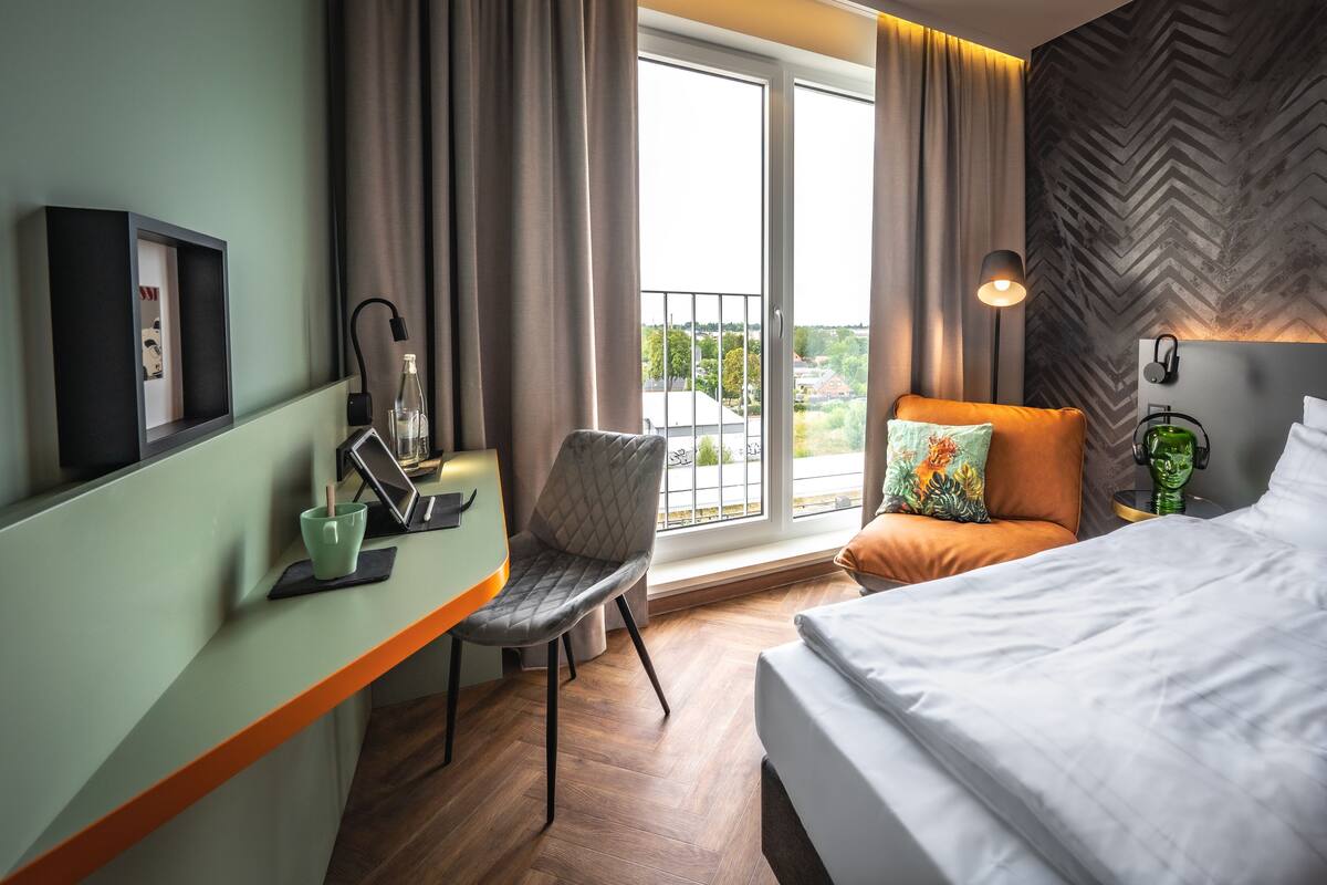 Een hotelkamer met een bed, een bureau met een computer, een stoel en uitzicht op buiten.