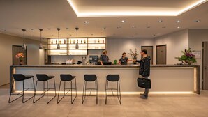 Een moderne receptie met een bar, barkrukken en een balie waar personeel gasten bedient.