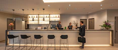 A modern reception area with a bar, bar stools, and a counter where staff are serving.