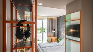 Een moderne hotelkamer met een bed, een televisie, een boekenkast met hoofdtelefoons en uitzicht op de stad.