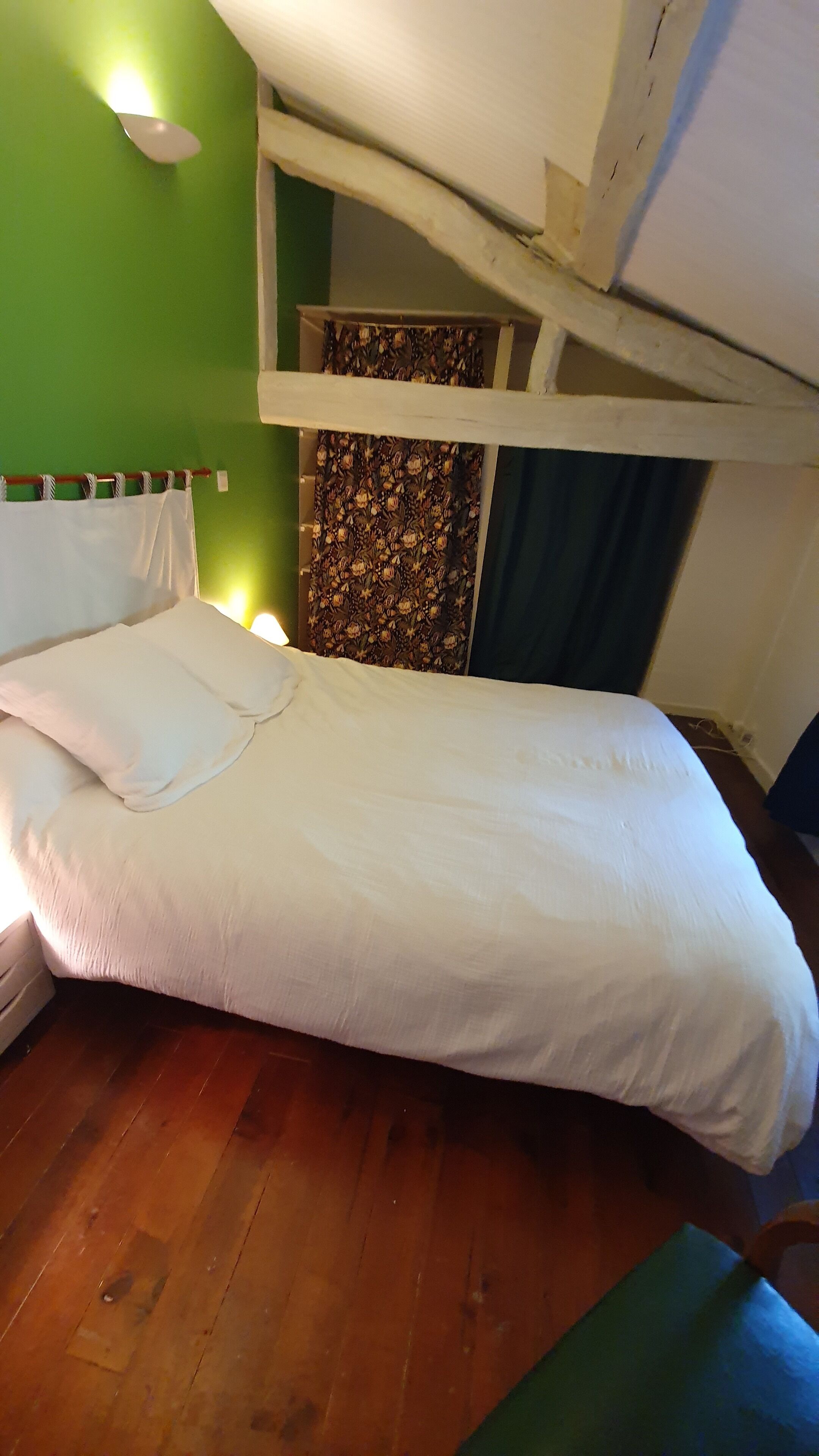 A single bed with white bedding in a room with green walls and wooden flooring.