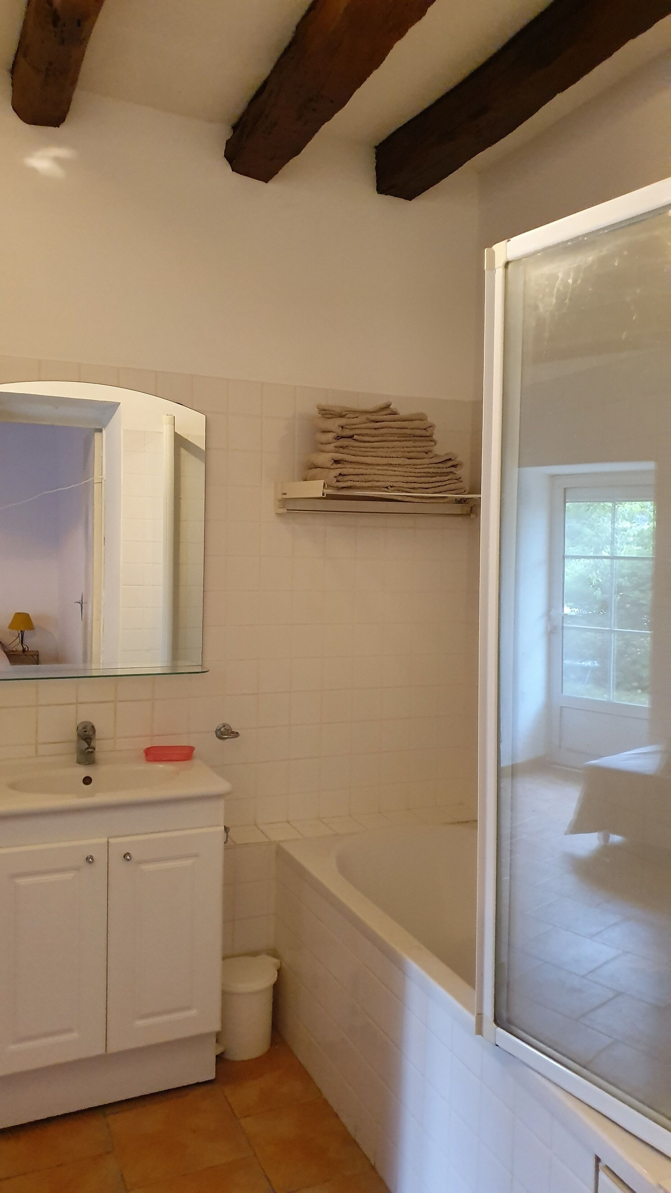 Een badkamer met een witte wastafel, spiegel en een bad met raam.
