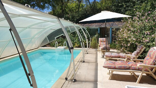 Una piscina amb una estructura de vidre, envoltada de gandules i una zona de seients coberta.