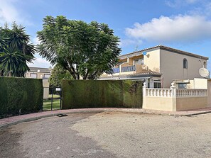 A residential property with a paved driveway, a neatly trimmed hedge, and a large tree providing shade. - Elegant terraced house in a fantastic south position in Els Poblets (Denia)