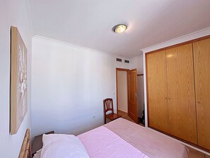 Een slaapkamer met een bed, een houten garderobe, een stoel en een plafondlamp.