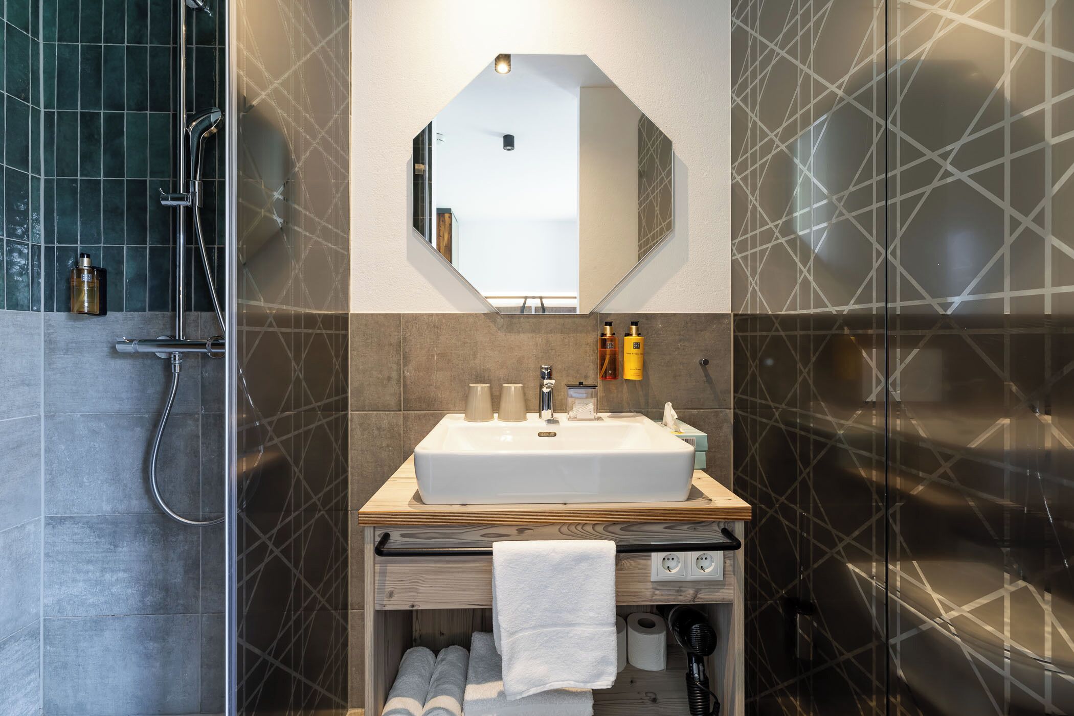 Un baño con un espejo grande, un lavamanos, una ducha y un perchero para toallas.