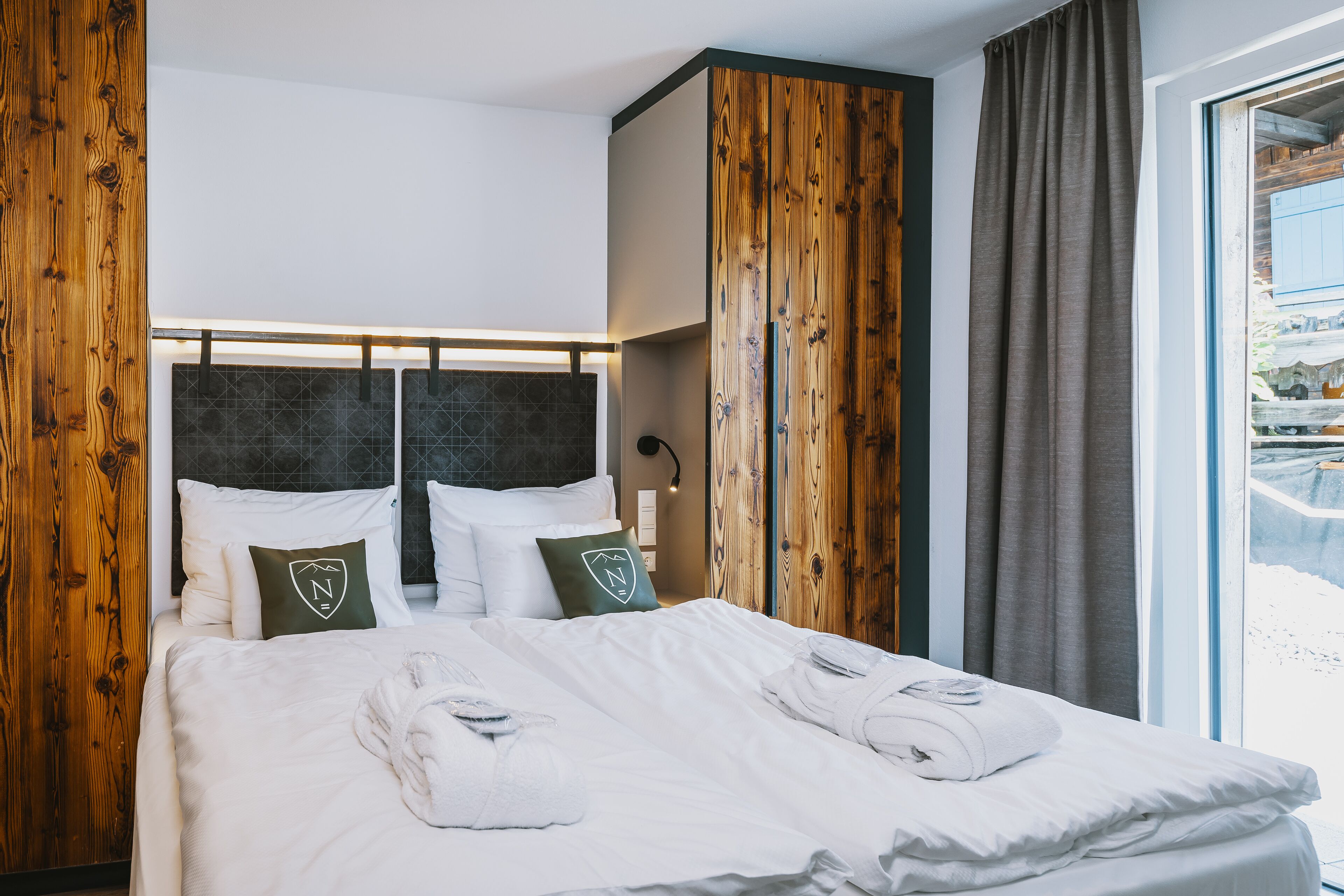 Habitación de hotel con cama grande, paneles de madera, vistas a un paisaje nevado y una ventana con cortinas.