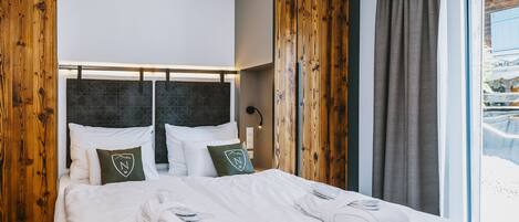 Habitación de hotel con cama grande, paneles de madera, vistas a un paisaje nevado y una ventana con cortinas.