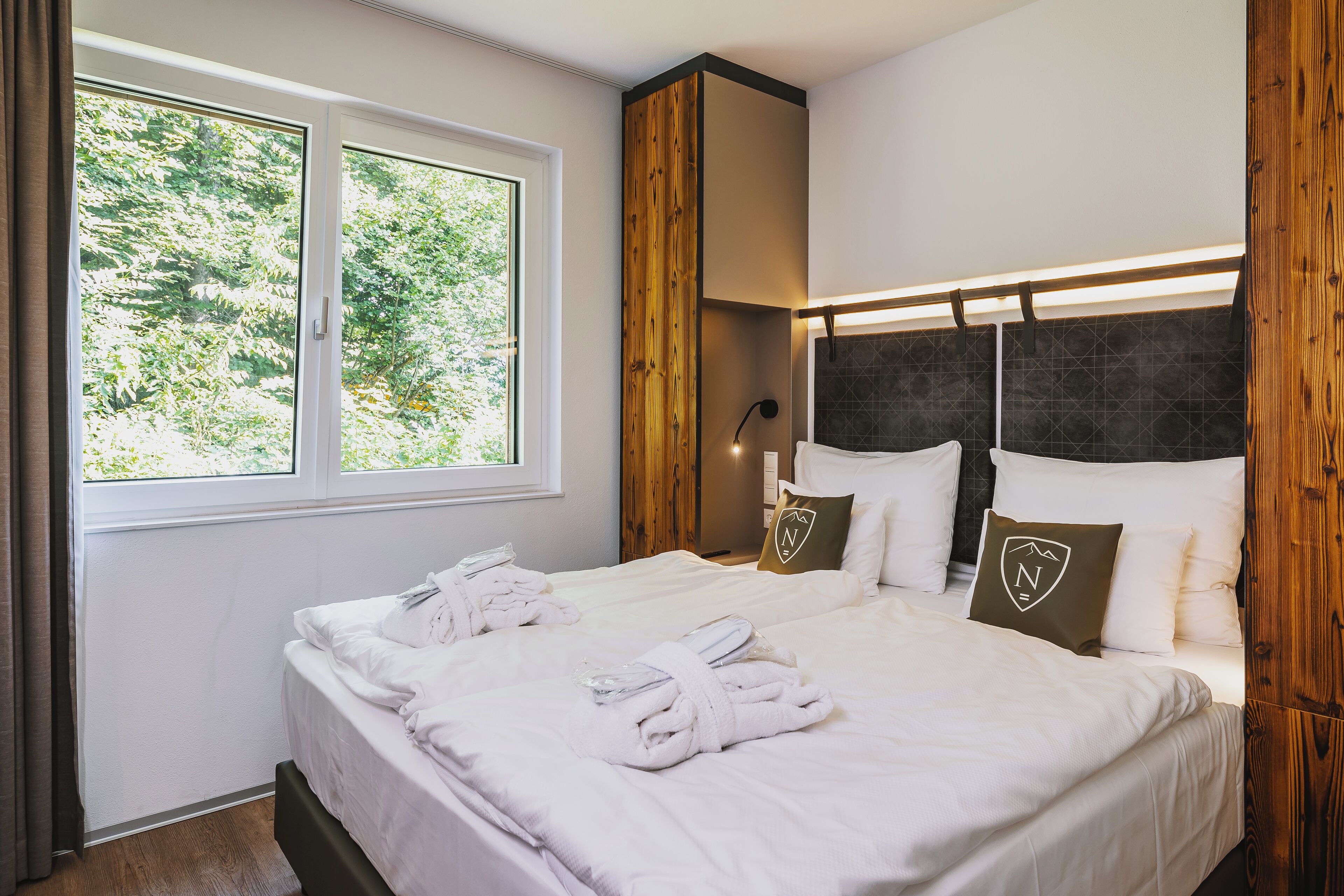 A neatly made bed with towels, a window with curtains, and a wooden headboard.