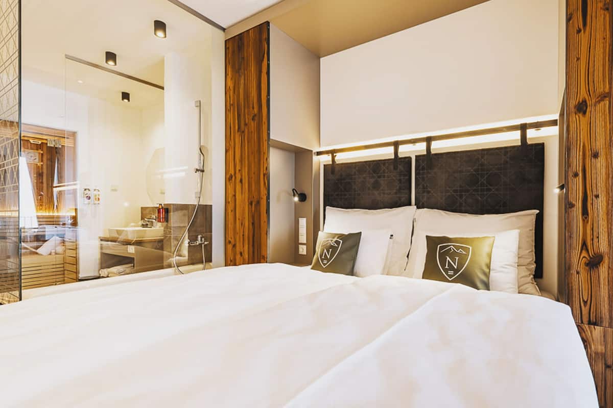 A hotel room with a large bed, wooden paneling, and a modern bathroom with a glass shower enclosure.