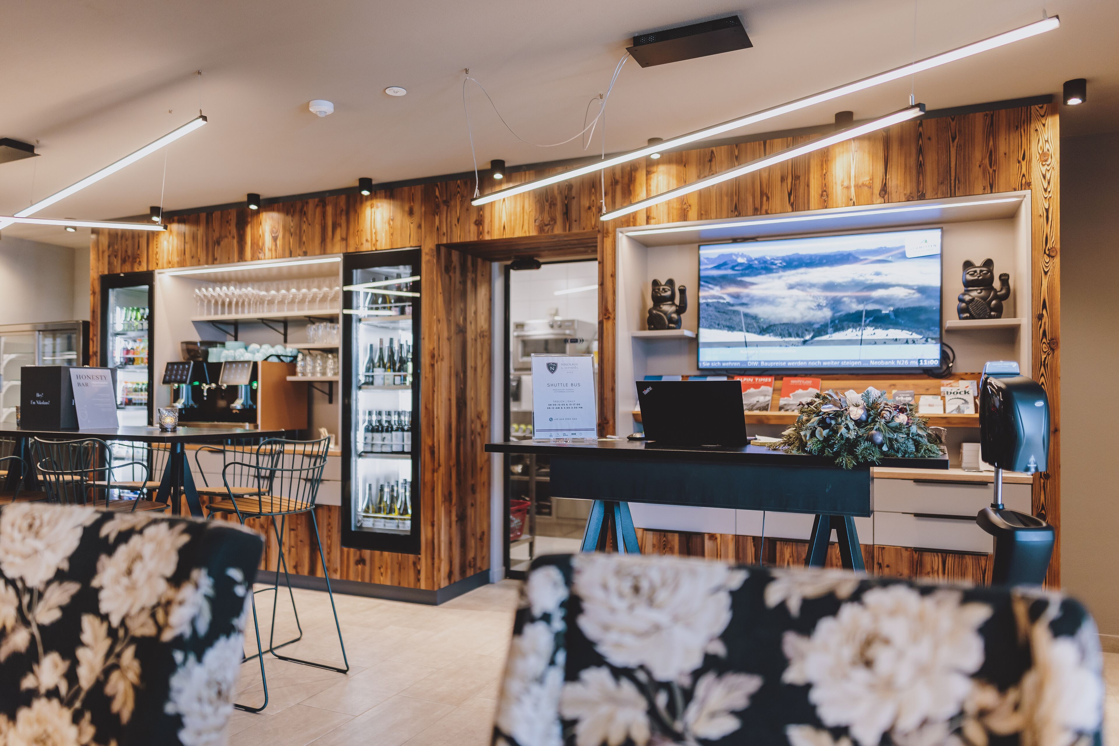A modern hotel lobby with wooden accents, a seating area, a bar, and a large TV screen displaying a snowy landscape.
