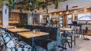 Ein modernes Café mit Holztischen, gepolsterten Sitzgelegenheiten, hängenden Pflanzen und einer Bar.