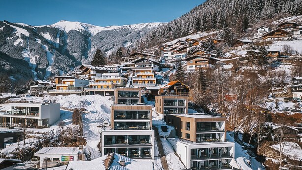 Eine verschneite Bergstadt mit modernen Gebäuden, darunter ein Hotel mit mehreren Etagen und Balkonen.