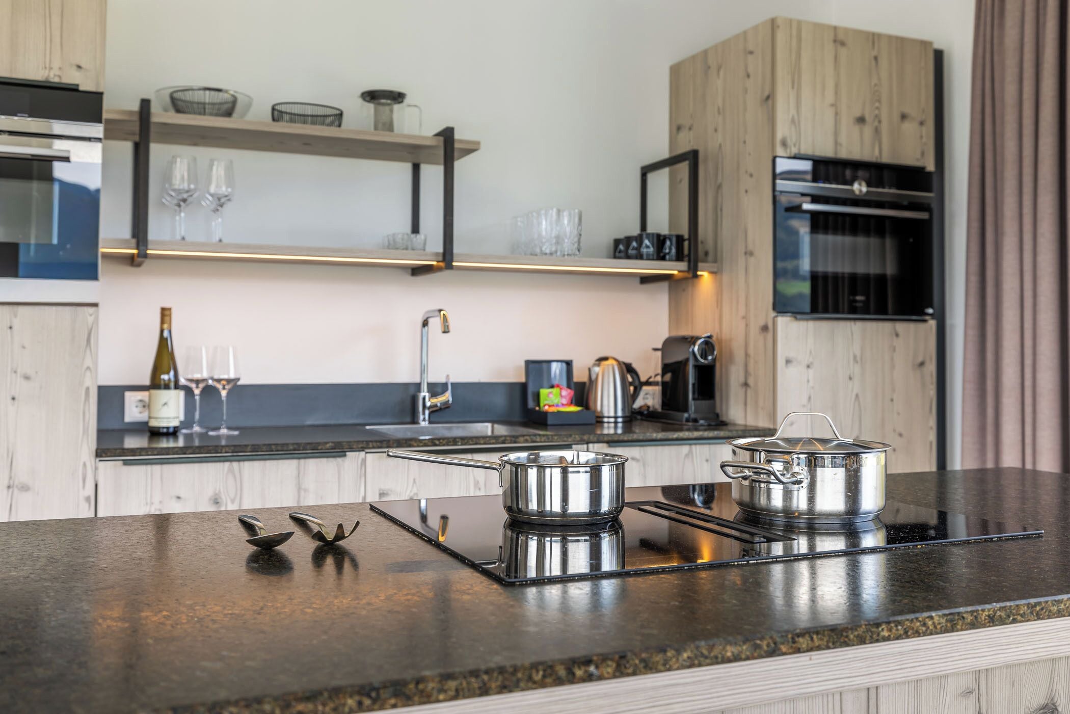 A modern kitchen with a built-in stove, a sink, and a wine glass on the counter.
