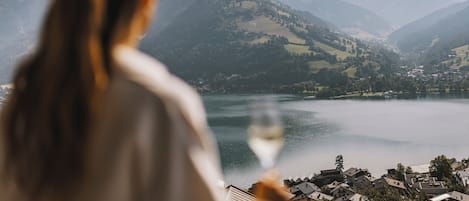 Una persona sosteniendo una copa de vino con vista a un lago y montañas al fondo.