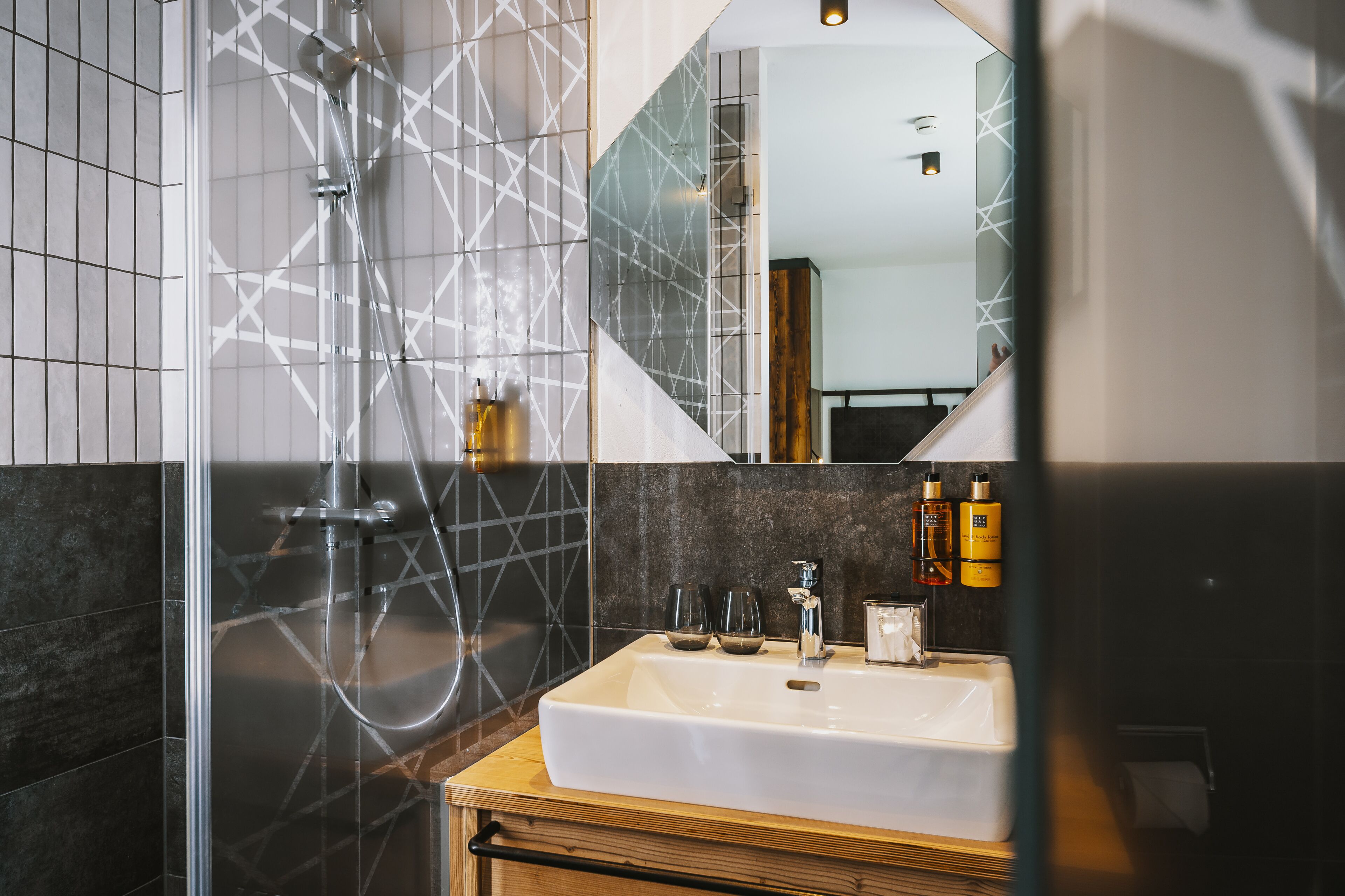 Un baño moderno con ducha acristalada, un lavabo blanco y un espejo que refleja el ambiente.
