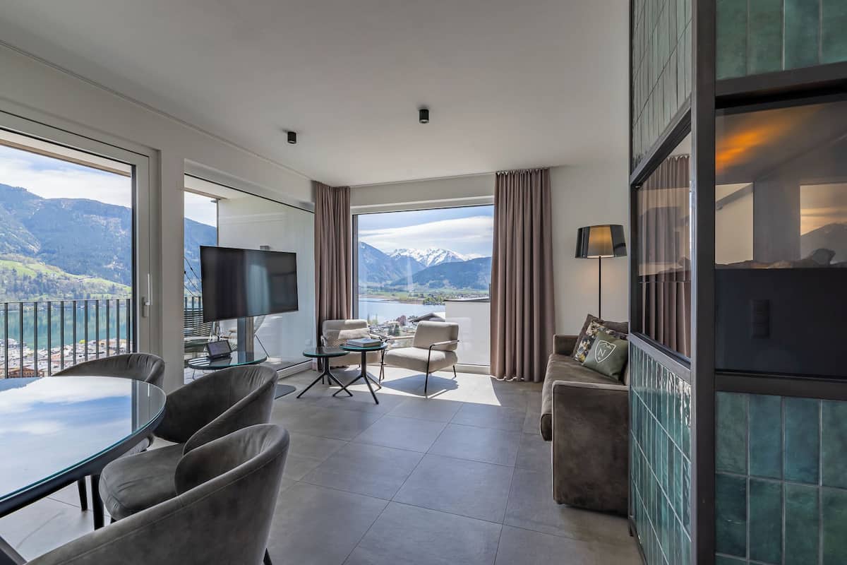 A modern hotel room with a large window, a flat-screen TV, a glass table, and a sofa.