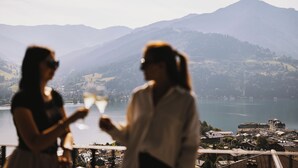 Zwei Personen blicken auf eine malerische Aussicht mit See und Bergen.