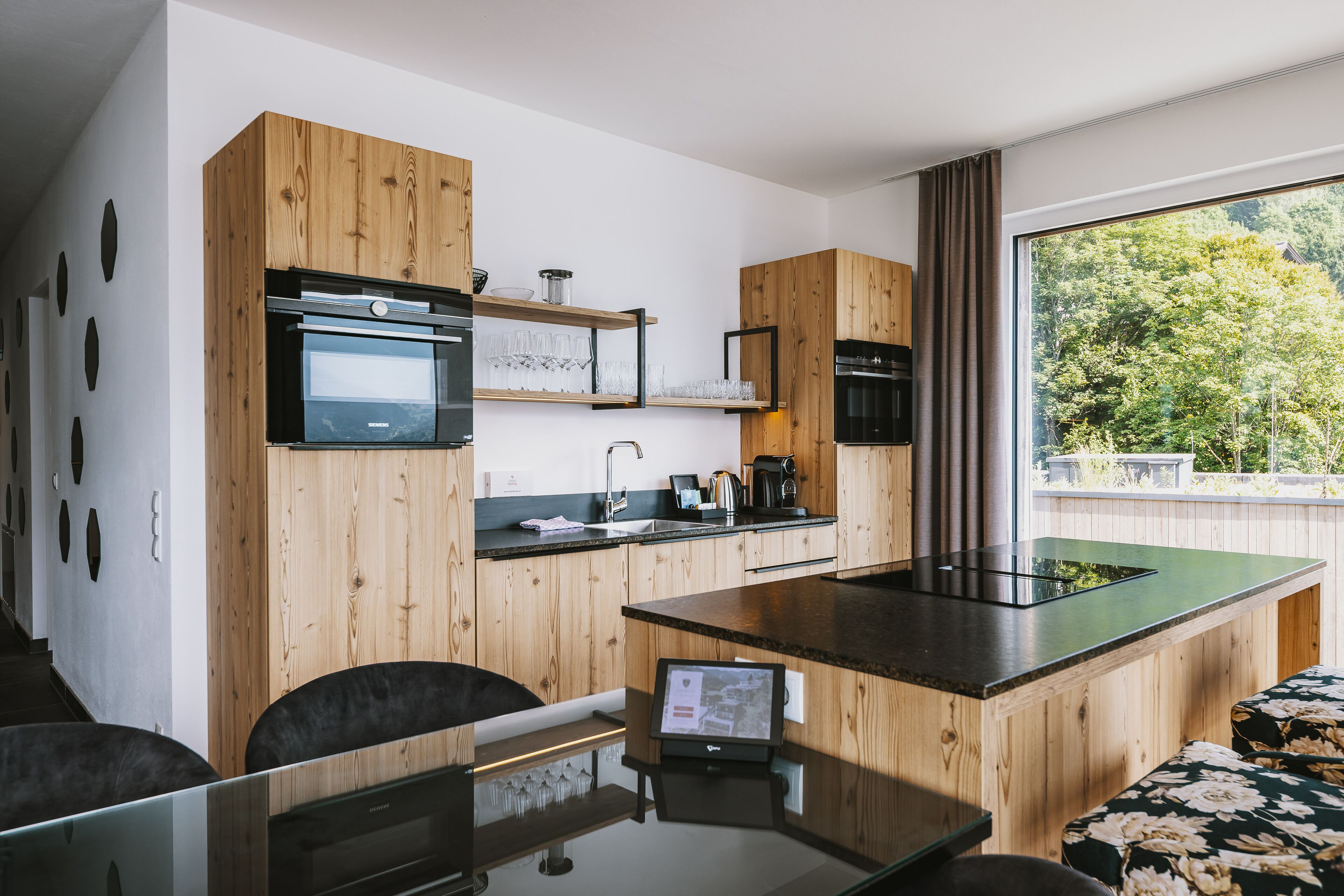 Eine moderne Küche mit Holzausstattung, einem eingebauten Ofen und einem großen Fenster mit Blick auf Grünflächen.