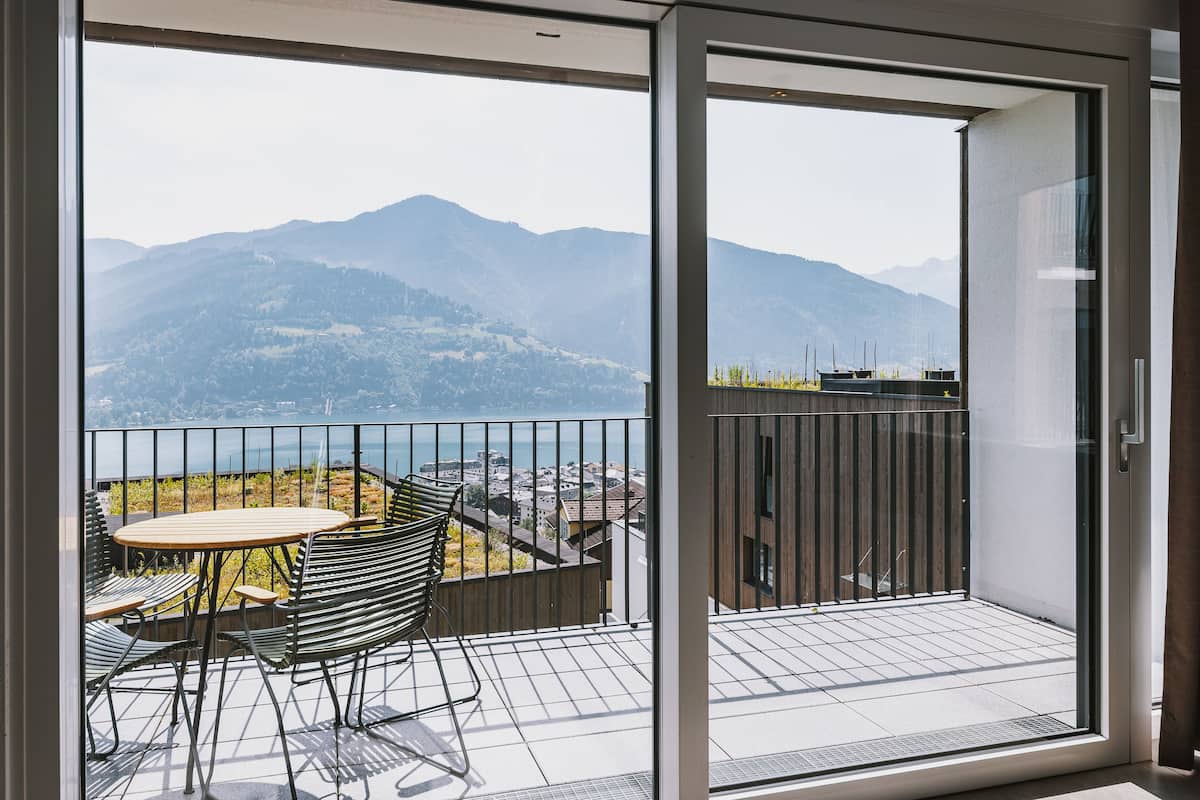 A balcony with a table and chairs, offering a view of mountains and a body of water.