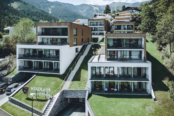 A modern multi-story residential building with a staircase leading to the upper floors, surrounded by lush greenery and mountains. - Nikolaus by AvenidA Zell am See (Zell am See)