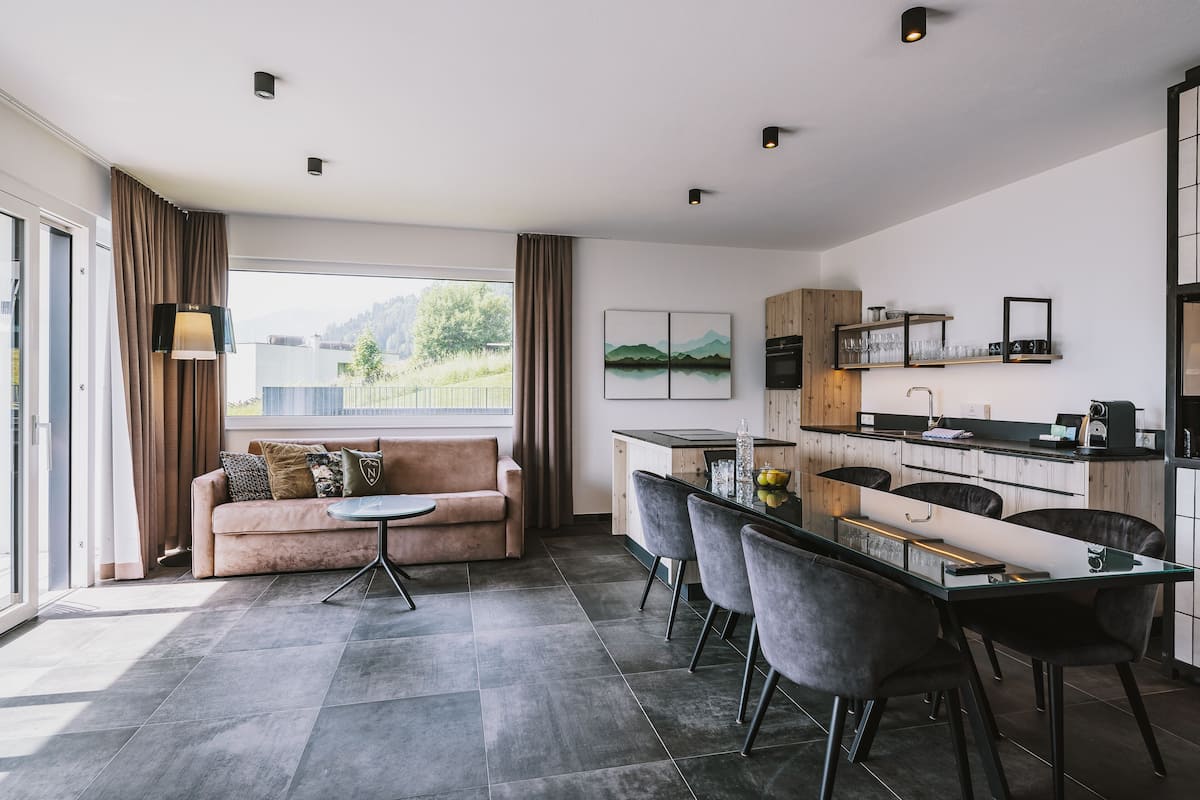 A modern kitchen with a dining area, a sofa, and a large window.