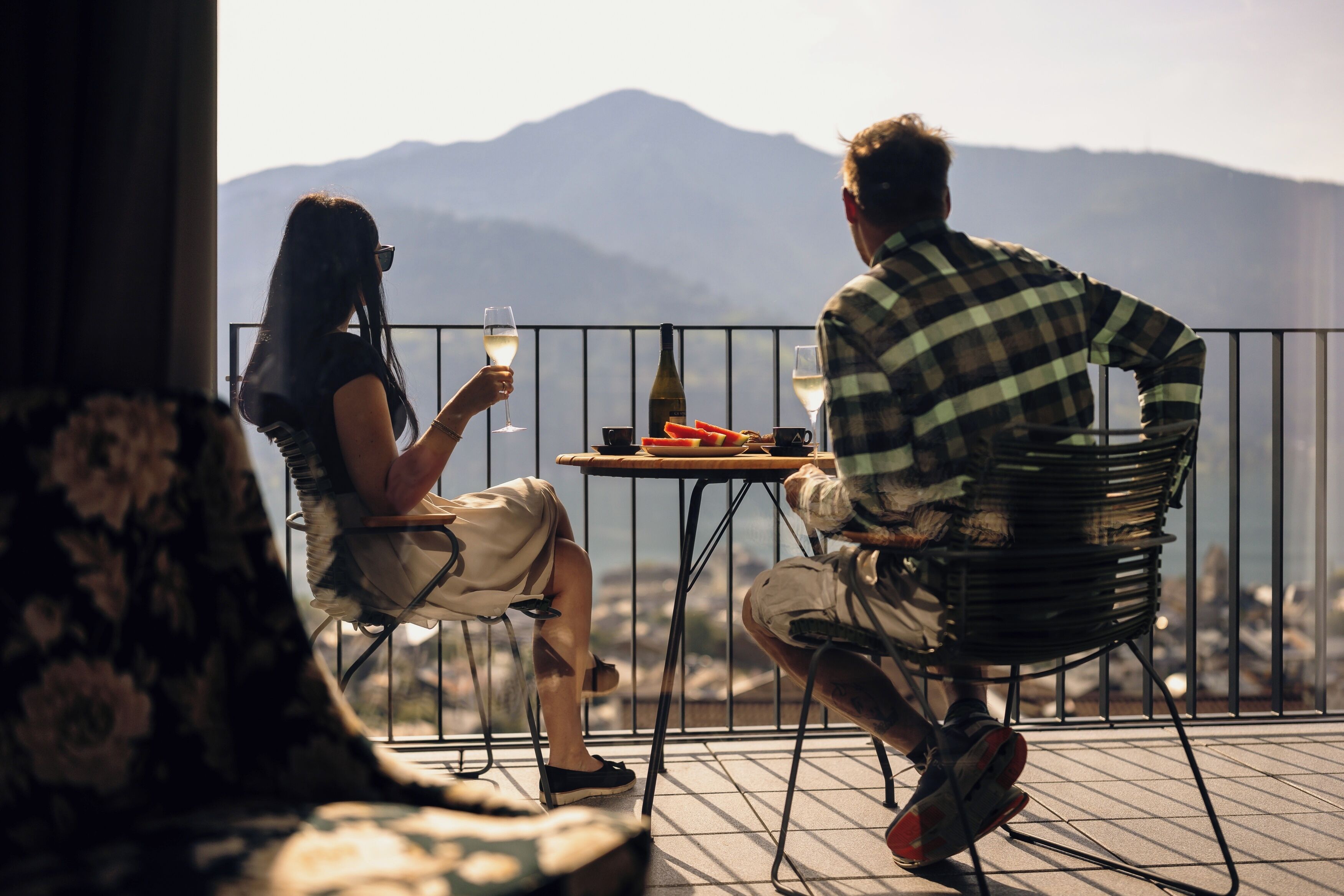 Two people seated at a table with a mountain view, a bottle, and a plate of food.
