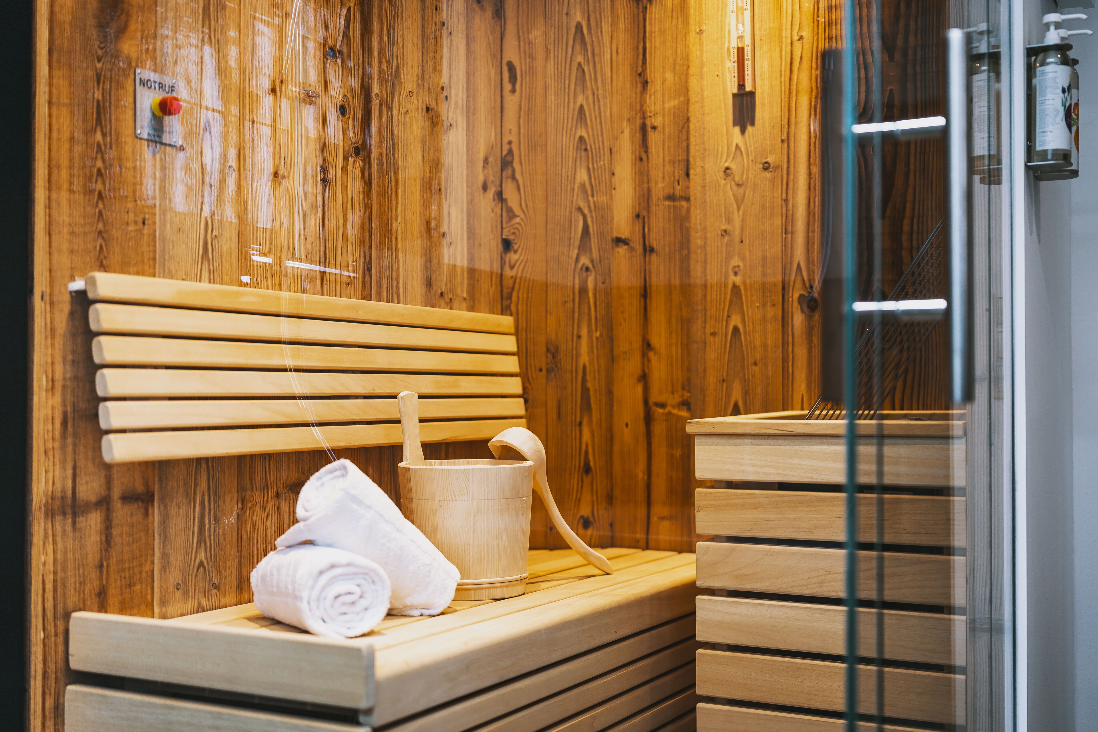 A wooden sauna with benches, a wooden bucket, and a towel.