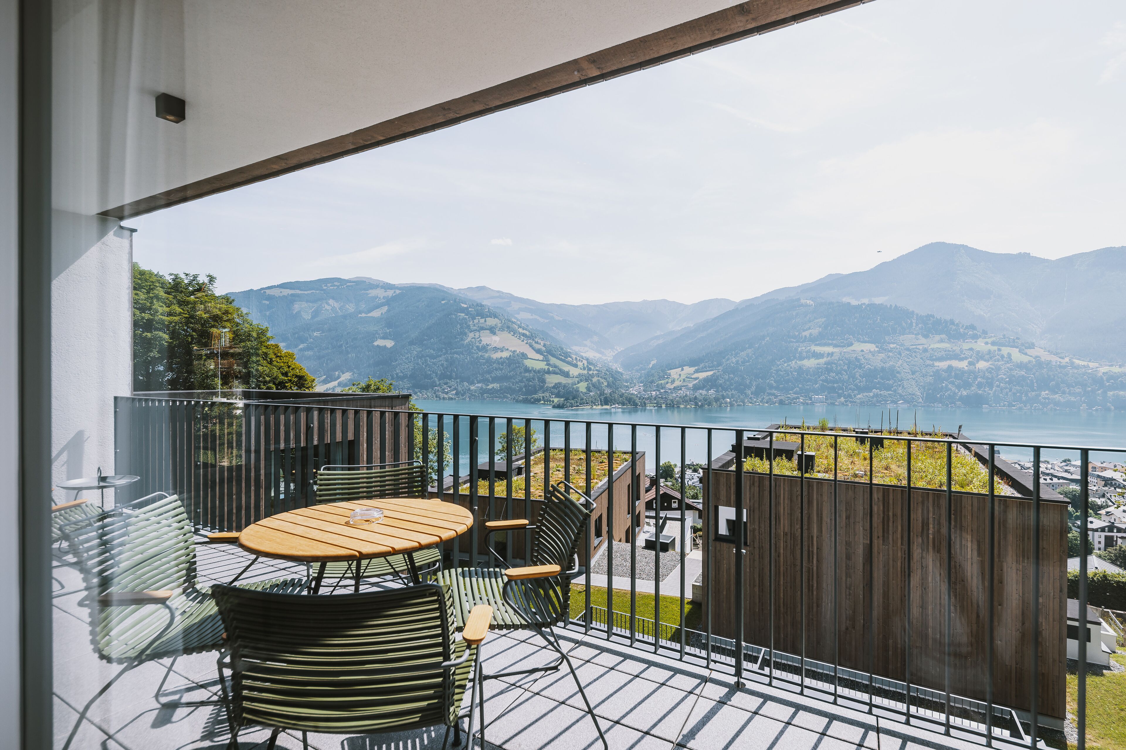 A balcony with a table and chairs, overlooking a mountainous landscape and a body of water.