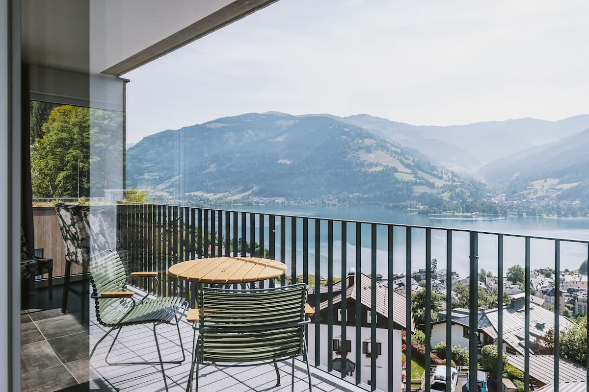 A balcony with a table and chairs, overlooking a lake and mountains.
