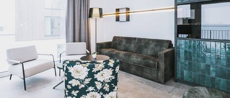 A modern living room with a sofa, two armchairs, a floor lamp, and a view of the city through large windows.