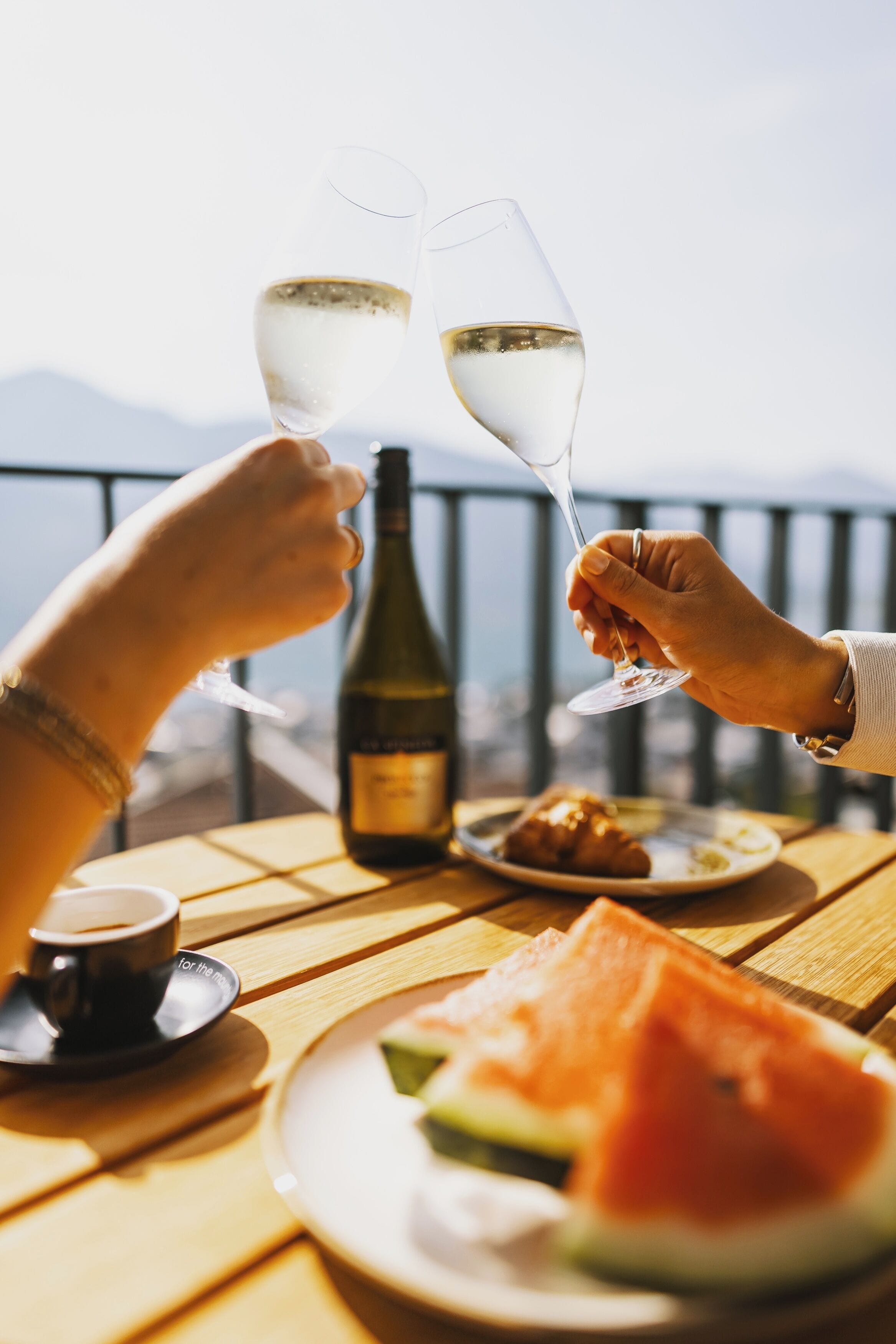 A table with a bottle of wine, a glass of wine, a plate of food, and a cup of coffee.